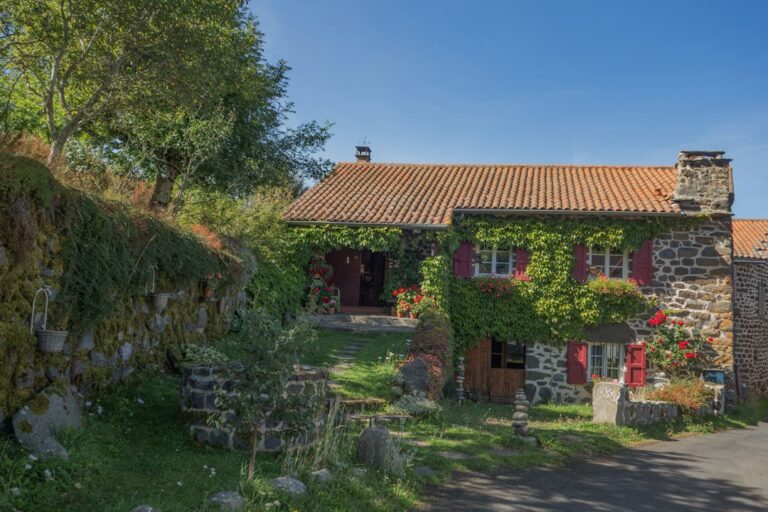 Maison en pierre, volets rouges et végétation en façade